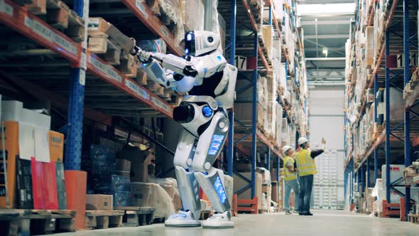 Warehouse Robot Scanning Barcodes on Cardboard Boxes with Two Workers in the Background