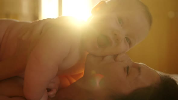 Young Mother Caressing and Kissing His Newborn Baby Kept By Mother in Arms in Kitchen at Home in the