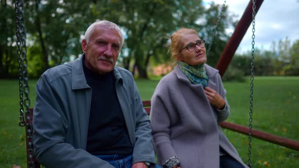 Lovely Senior Couple On A Swing In A Park Relaxing. Zoom Out