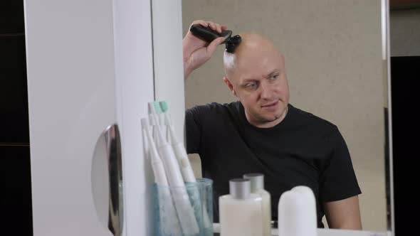 A Bald Man Shaves His Head with an Electric Razor in the Bathroom