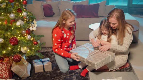 Mother with Daughters Opening Gifts Near Christmas Tree