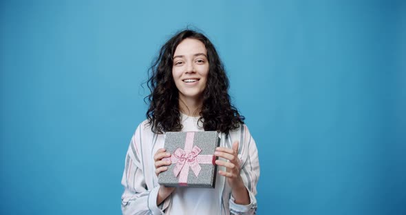 A Young Woman Opens a Gift in a Beautifully Packaged Box on a Blue Background