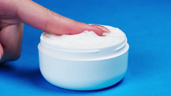 Female Hand Taking Moisturizing Cream for Face or Body on Blue Background