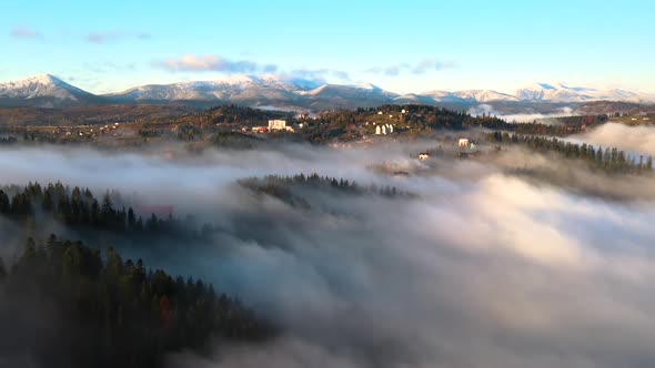 Aerial view of a small village houses on hill top in fall foggy mountains at sunrise.