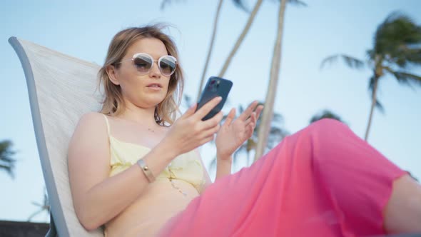 Smiling Young Woman Customer Holding Smartphone Sitting at Hawaii Island Resort
