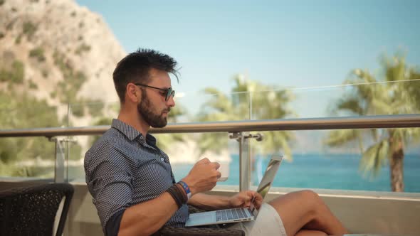 Businessman In Sunglasses. Businessman Drinking Tea On Vocation Resort. Man Sitting On Cafe At Sea