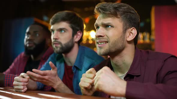 Caucasian and Black Male Friends Watching Football Game in Bar, Team Losing