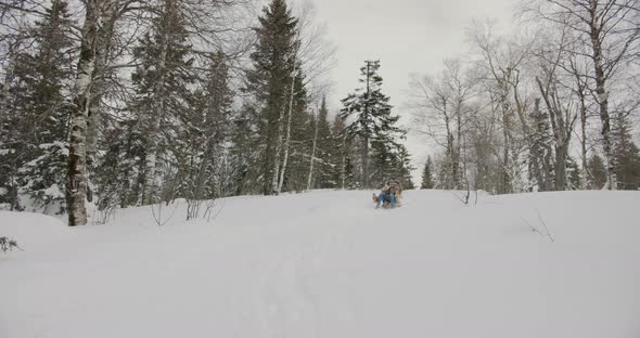 Man and Woman Sliding Down the Hill in Sled Laughing Having Fun Together in Winter Forest