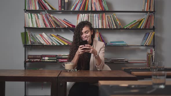 Girl Texting On Phone With Book Shelf In Background At Cafe Restaurant