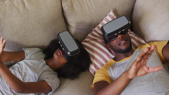 African american daughter and her father lying on couch wearing vr headsets