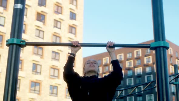Young Woman in Morning Practices Pullups on Bar in Black Hoodie with Pigtail
