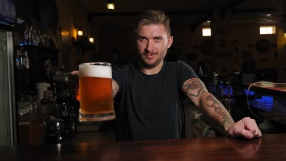 Male Bartender Stretching Out Glass with Beer While Standing at the Bar Counter