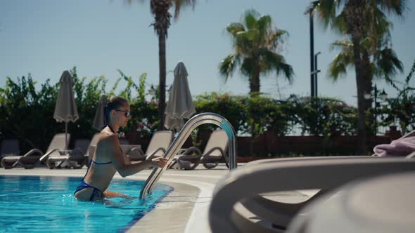 Attractive Woman in Blue Swimsuit and Sunglasses Coming Out of the Pool