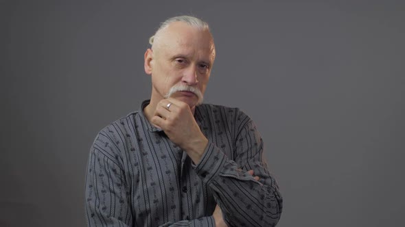 Concentrated Elderly Man Touches and Strokes Mustache