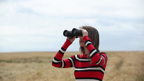 Woman in striped sweater looking in binocular in wheat field