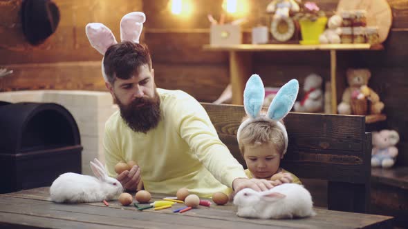 Father and Son Wearing Easter Bunny Ears. Funny Faces. Happy Family Painting Eggs. White Rabbit