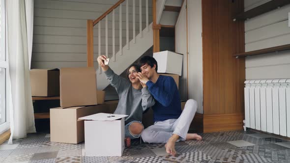 Young Man and Woman Are Taking Selfie with Smartphone Making Heart Shape with Fingers Sitting on