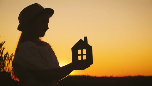 Girl Holding Paper House on Field During Sunset. Dream, Family and Home Concept.