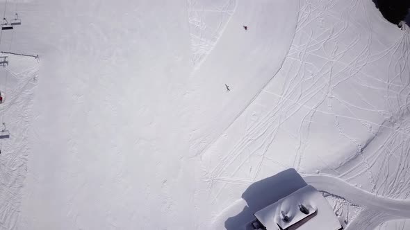 Aerial of ski resort at sun mountains with pine forest. Skiers ride down on snow slope at lifts. Win