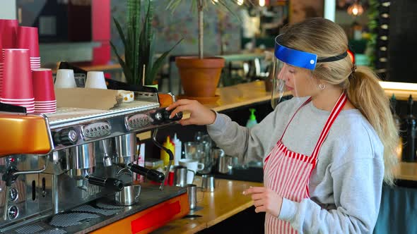 Barista Woman is Cleaning Coffee Machine in Restaurant Wearing Plastic Face Shield From Covid