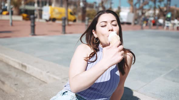 Cheerful brunette woman eating ice cream while sitting on the bench
