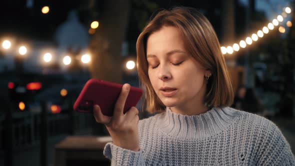 Young Woman Walking in the Street Evening Makes Short Phone Call By Speakerphone Using Telephone