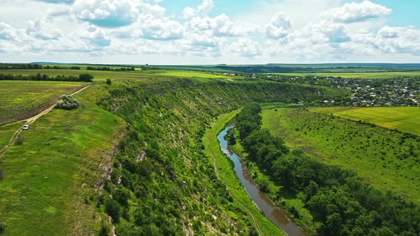 Aerial drone view of a valley in Moldova. River, a lot of greenery, cloudy sky, village