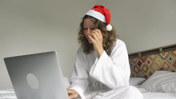 Happy Young Woman Sits on Bed Rejoices Looking Into Laptop