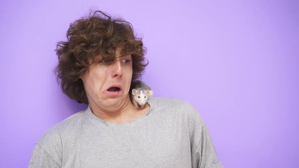 A Young Guy with a Lush Hairstyle on an Isolated Background Looks Scared at a Rat That Crawls on His