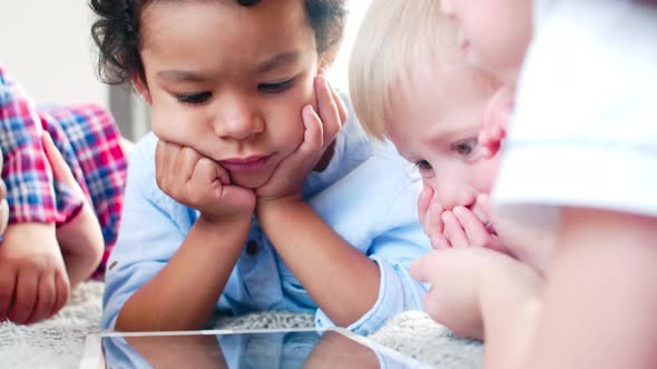 Interracial Little Children Lying on Bed and Watching Cartoon on Tablet