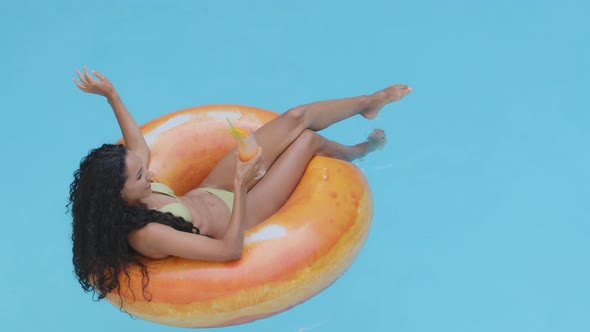 Attractive Slim Girl Model with Long Tanned Legs Resting Drinks Cocktail Lies in Orange Inflatable