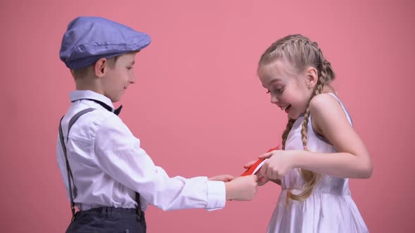 Little Boy in Formal Wear Presenting Birthday Gift Card to Happy Surprised Girl