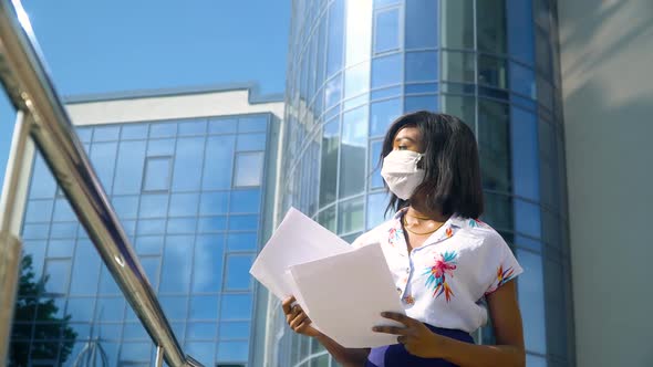 African American Young Businesswoman with Documents in a Protective Mask Looking at the Camera Near