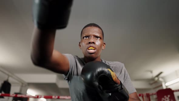 Young African Man Boxer Punching with Fists to Camera While Training on Ring at Gym