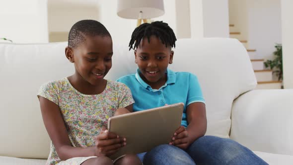African american boy and girl using digital tablet while sitting on the couch at home