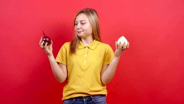 Cute and Slightly Fat Girl in a Yellow T-shirt with a White Onion in One Hand and a Red Onion in the