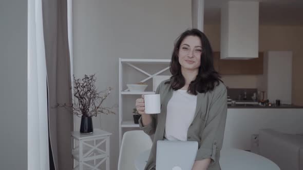 Young Attractive Cute Woman with a Cup of Coffee with a Laptop in Her Hands