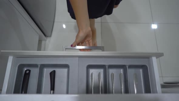 A Woman Walks To the Kitchen Cupboard and Takes a Spoon and Fork From the Drawer