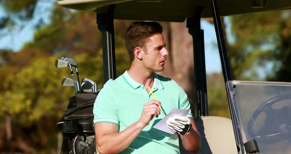 Golfer sitting in golf buggy writing on paper