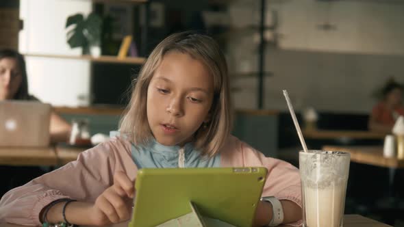 Little Girl Smile and Play in Tablet in Cafe Drink Milkshake and Dooing Homework, Working Girl Smile