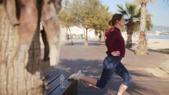 Woman Trains in the Park on a Bench Performing Lunges Squats on One Leg