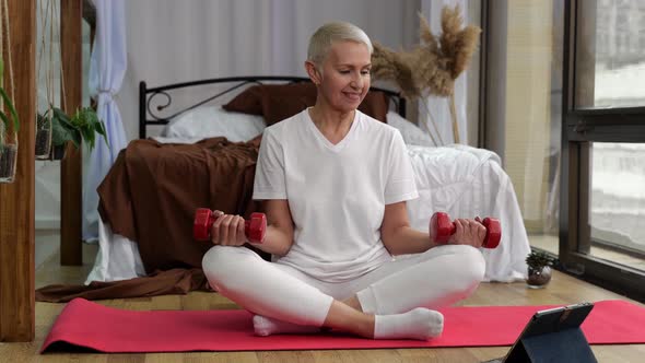 Senior Woman Doing Exercises By Lifting Dumbbells with Online Tutorial at Home