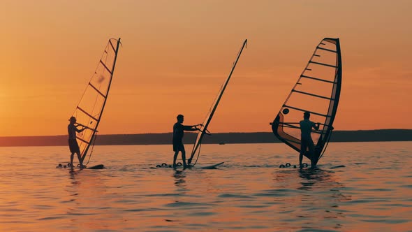 Group of Men Are Windsurfing in the Sea at Sundown