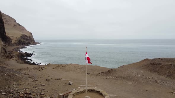 Drone video of a Peruvian flag post near a cliff edge on ocean coast. Drone flies over the flag and