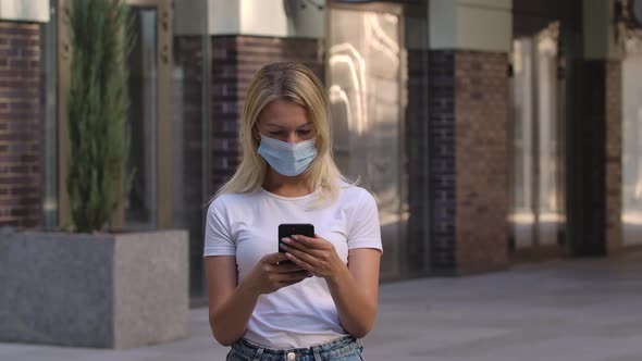 Portrait of Pretty Young Woman in Protective Medical Mask Is Texting Message on Her Smartphone