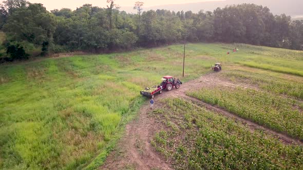 Aerial following tractor in corn fields with workers.