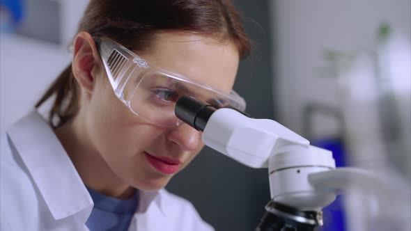 Young Female Chemical Laboratorian is Viewing Into Microscope Closeup of Face