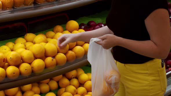 A Young Woman Stands in the Grocery Section of a Supermarket Picking Up Apples in a Weighing Bag