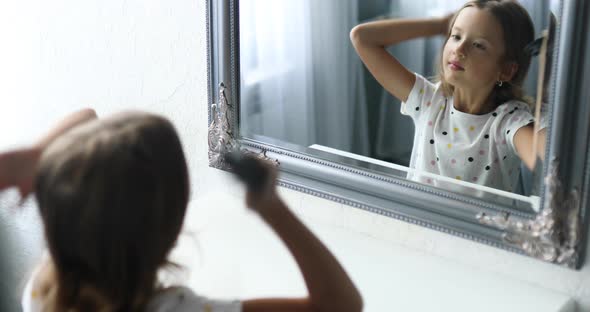 Pretty Little girl combing by herself hair in front of a mirror