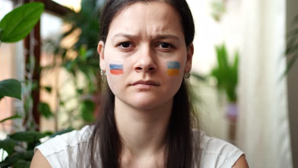 A Young RussianUkrainian Girl with the Flag of Ukraine and Russia on Her Face is Frowning Eyebrows